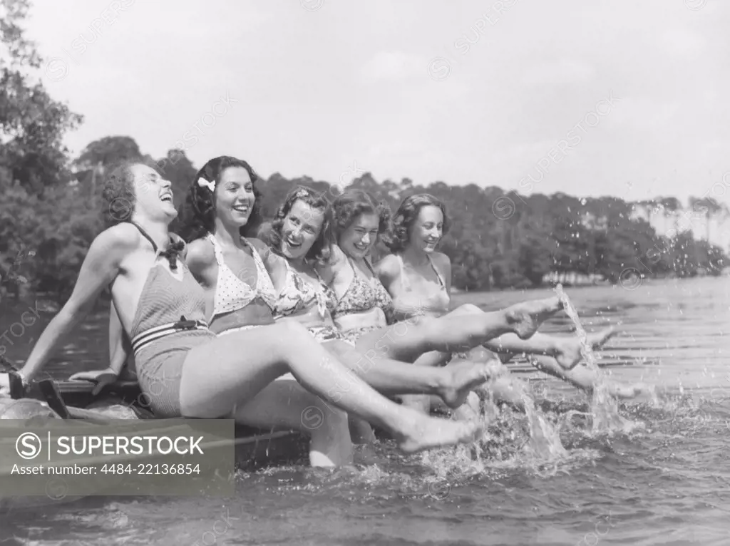 1930s summer. A group of young women on a summers day. They move their feet around in the water so it splashes. 