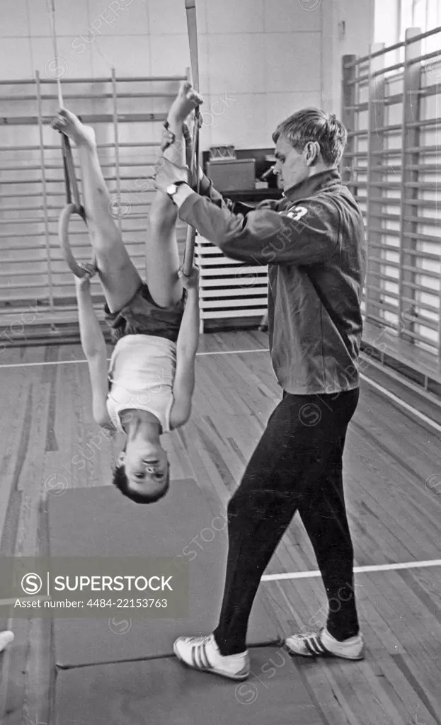 School gymnastics in the 1970s. A teacher is helping a young boy balancing during gymnastics class. Sweden 1970s