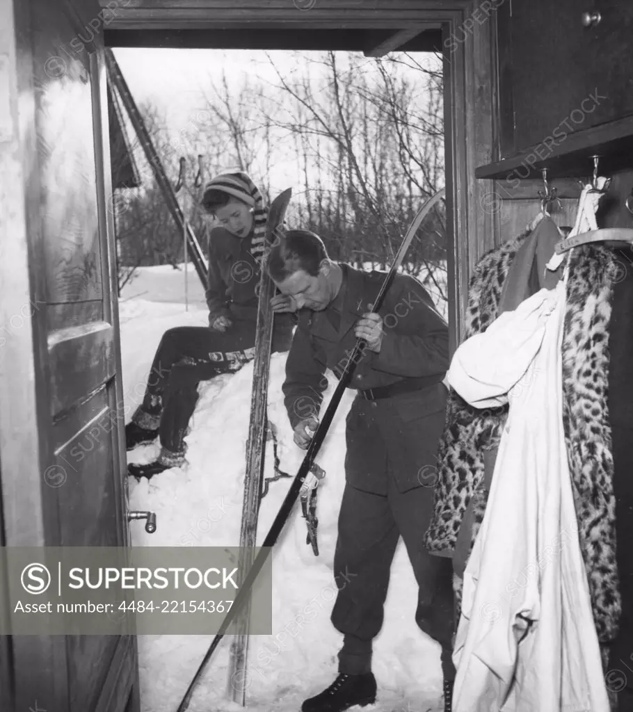 Winter in the 1940s. A young couple are going skiing and prepares the skis with ski wax to get better traction on the snow.  Sweden 1940s. Photo Kristoffersson 