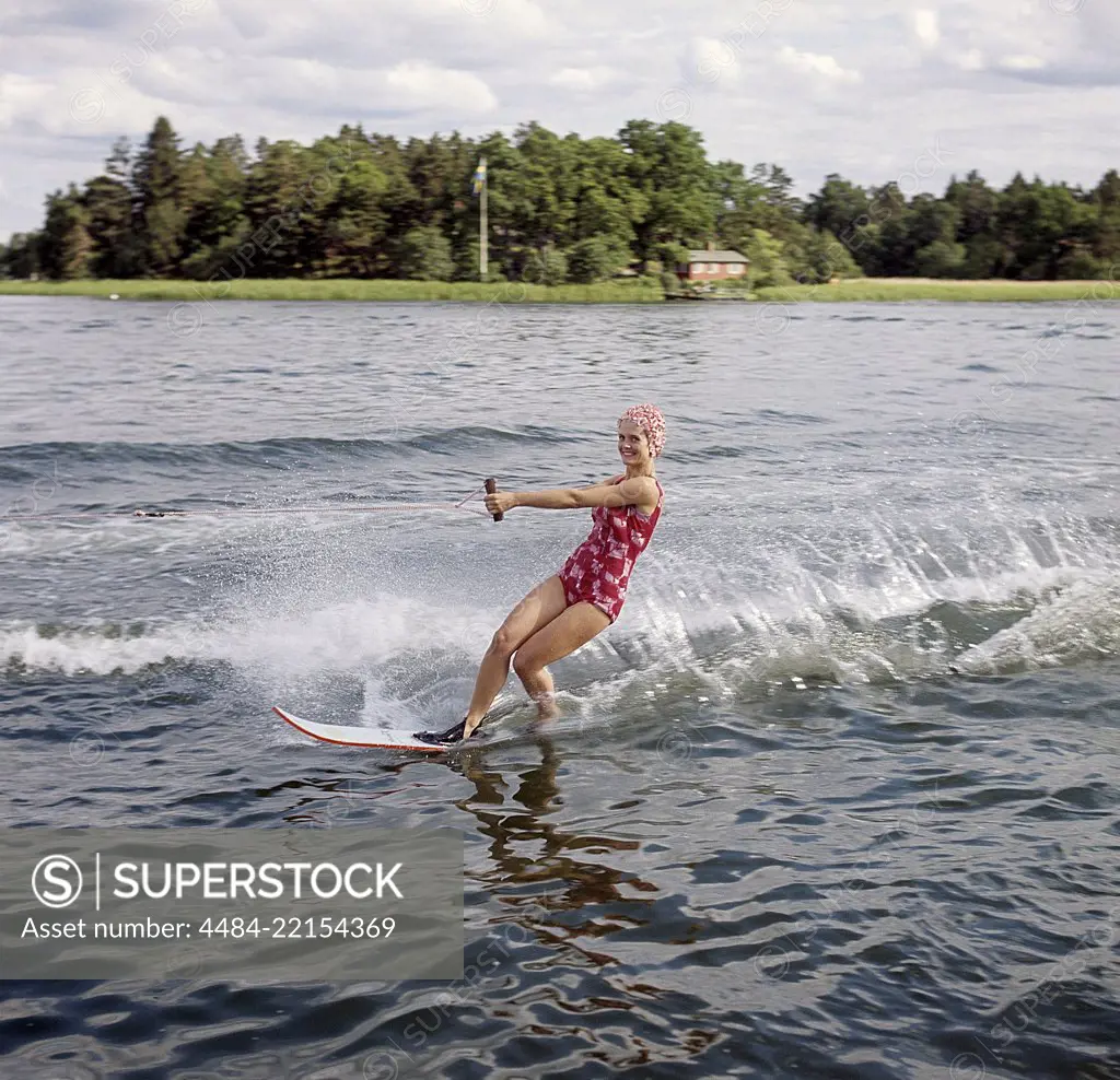 Waterskiing in the 1960s. A young woman in a patterned bathing suit passes the photographer on her waterskis. She has a typical bathing cap on. Sweden 1946 Photo Kristoffersson ref CV12-7