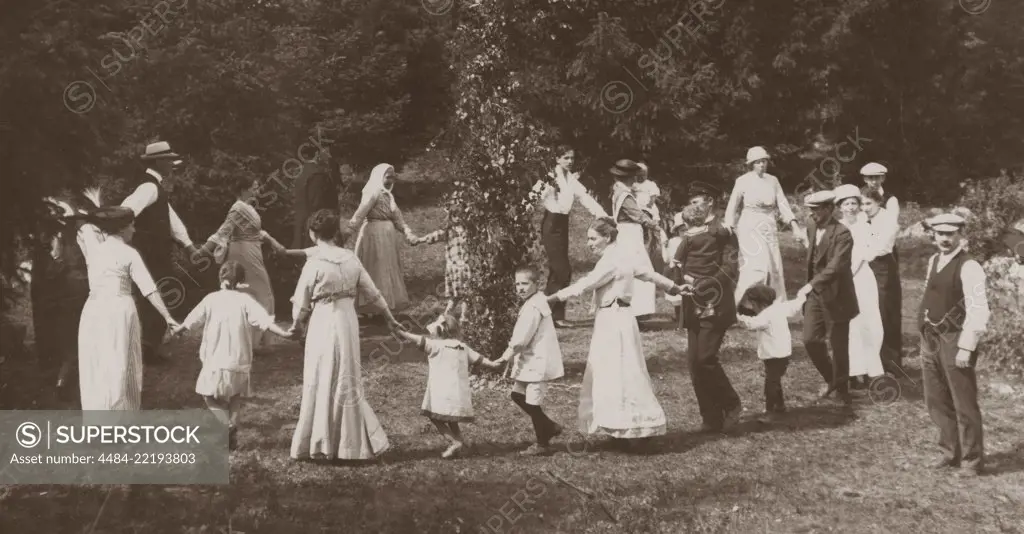 Midsummer tradition in Sweden. As a part of the festivities a Maypole is risen men, women and children gather to dance around it. Sweden at the beginning of the 20th century.