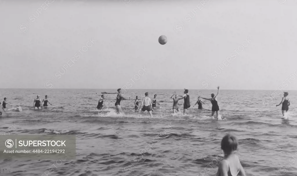 Summer in the 1920s. A group of people are playing ball in the water on a sunny day on the beach. Sweden 1920s