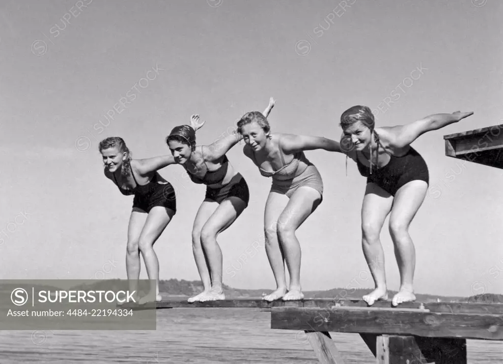 Swimming in the 1940s. A line of four women are standing ready to jump in the water on a summer's day. Sweden 1940s