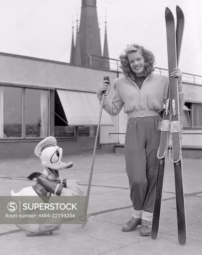 Winter sports in the 1950s. A young blonde woman with her skies, poles and shoes together with a Donald Duck figure. Sweden 1952. Photo Kristoffersson ref 179A-1