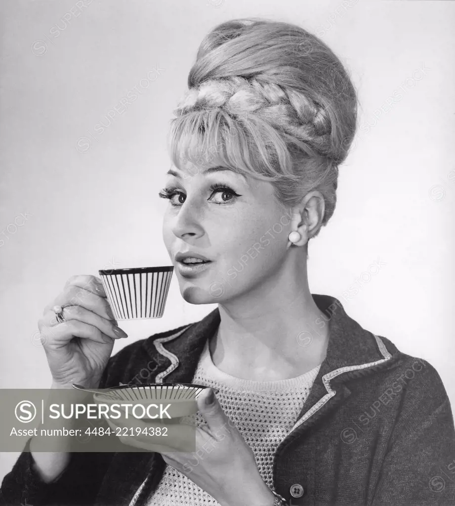 Coffee in the 1960s. A woman is drinking coffee from a coffeecup with a 1960s striped pattern. She has her hair in the typical Beehive hairstyle, in which long hair is piled up on the top of the head and giving some resemblance to the shape of a traditional beehive. Sweden 1962