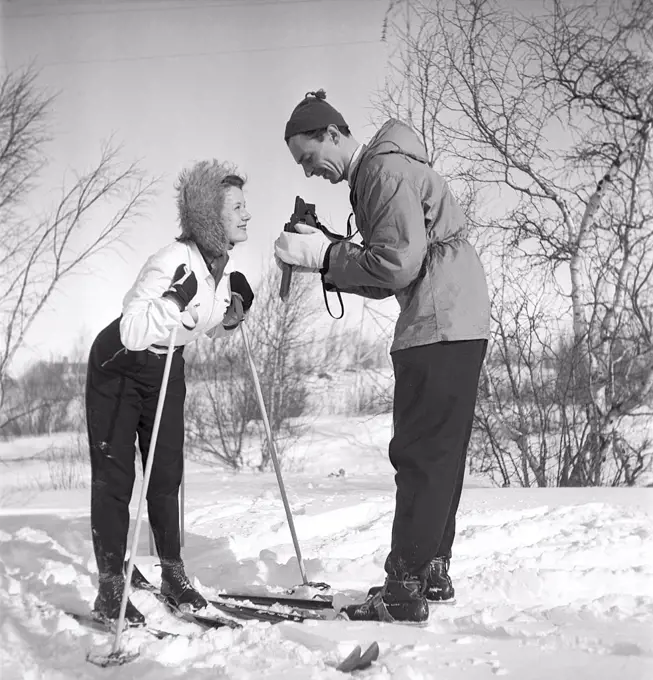 Winter in the 1940s. Actor Nils Kihlberg, 1915-1965 is pictured here with his wife Ann-Britt. He is taking pictures of her on their winter vacation. They are both wearing winter clothes and skis.  The camera is a Rolleiflex by german company Rollei.  Sweden 1943. Kristoffersson Ref D70-2