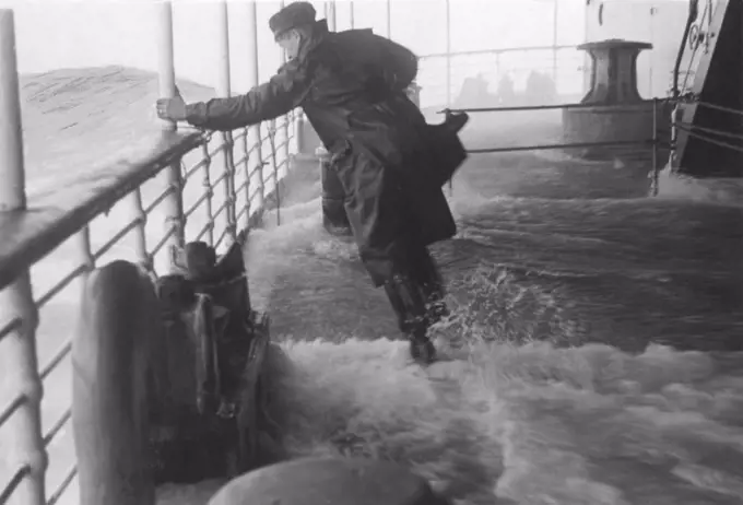 Rough weather at sea. A sailor is struggling to stand up straight on the ships deck as water and wind makes the ship turn and twist. Sweden 1940s