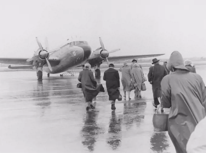 1950s vacation. A group of people are walking in the pouring rain towards the waiting plane bound for Spain. Sweden 1951. ref 385