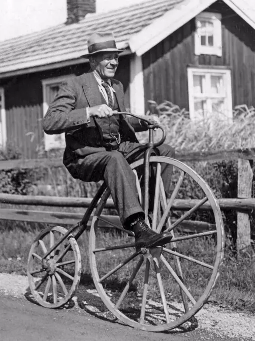 Penny farthing bicycle. A man is riding a penny-farthing bicycle he has made himself with wooden wheels both front and back. Sweden 1940s