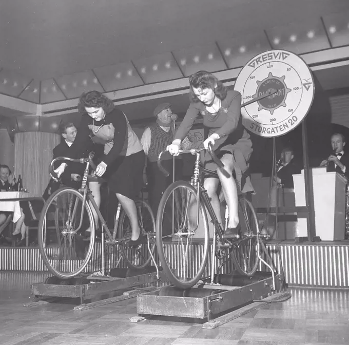 1940s women on a bicycles. Two young women are participants in an competition on who is reaching the highest speed when riding the bikes on a machine that measures it. It is the norwegian company Gresvig who is the organizer of the event. The company was Norways largest manufacturer of skis and bicycles, and their top bicycle model was The Diamond. Sweden 1940s. Photo Kristoffersson AX21-8