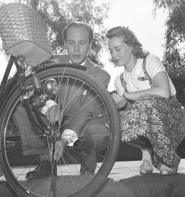 1940s couple with a bicycle. Actor Willy Peters is seen here pumping air into the tire of a womans bicycle while she is sitting beside him and looking. Sweden 1940s. Photo Kristoffersson E50-3