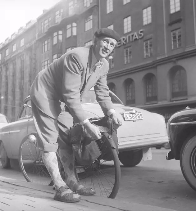 1950s man with his bicycle. A man in has parked his bicycle and balancing it on the kerb. He puts a chain around the back wheel, unabling it from being stolen. Notice the registration sign on the bicycle that was a mandatory item at this time. Sweden 1950s. Photo Kristoffersson ref BP57-5