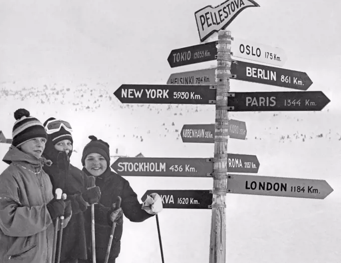 Winter in the 1960s. A group of young skiers is standing in front of signs where the distance to the cities like New York and London are listed in Km. Sweden 1967