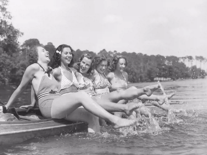 1930s summer. A group of young women on a summers day. They move their feet around in the water so it splashes. 