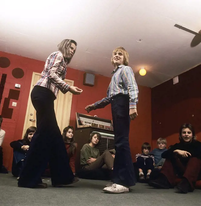 Teenage party in the 1970s. A group of teenagers have arranged a party and a boy and a girl is dancing to the music from the jukebox. Notice the wide legged jeans type that was typical of the decade. Sweden 1970s. Photo Kristoffersson
