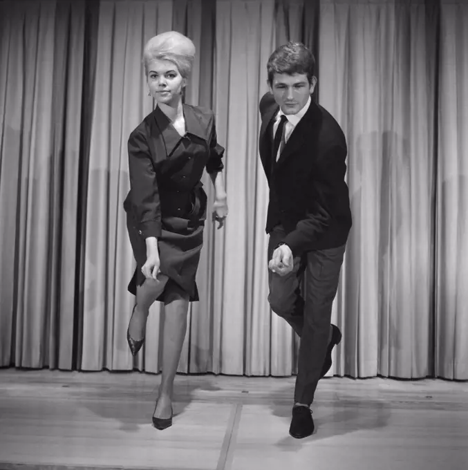 Dancing in the 1960s. The dance Hully Gully is being made popular and here are men and women dancing the new craze. Hully Gully was a type of unstructured line dance and consisted of a series of steps and was relatively simple and easy to execute. Hully Gully can be seen performed by actor John Belushi in the film Blues Brothers. Notice the typical BeeHive hairdo on the girl.