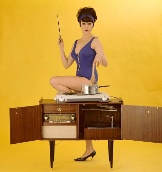 1960s bikini. A young brunette in a swimsuit. Pictured when cooking on top of a combined radio record player. Sweden 1960s. Pirkko Mannola