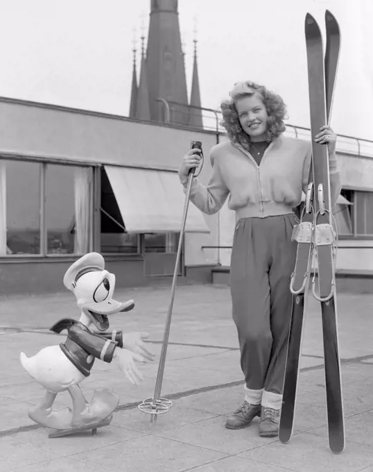 Winter sports in the 1950s. A young blonde woman with her skies, poles and shoes together with a Donald Duck figure. Sweden 1952. Photo Kristoffersson ref 179A-1