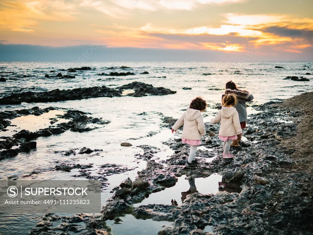 anonymous little girls from behind standing by the beach on rocks looking at the sea on a winter day