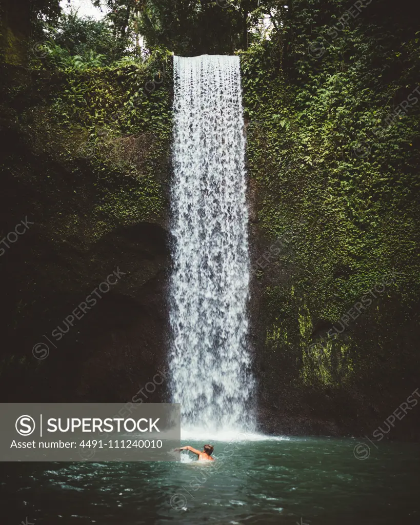 Side view of man swimming in clear water of lake with waterfall on background, Bali