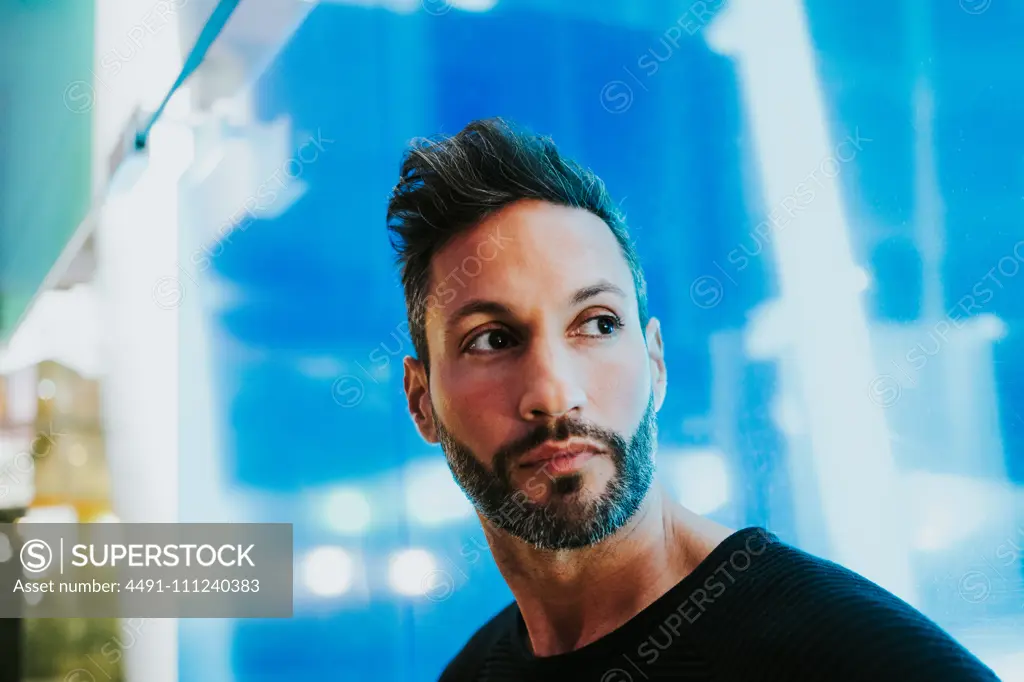 Adult handsome elegant serious bearded male looking away near blue glasses on blurred background