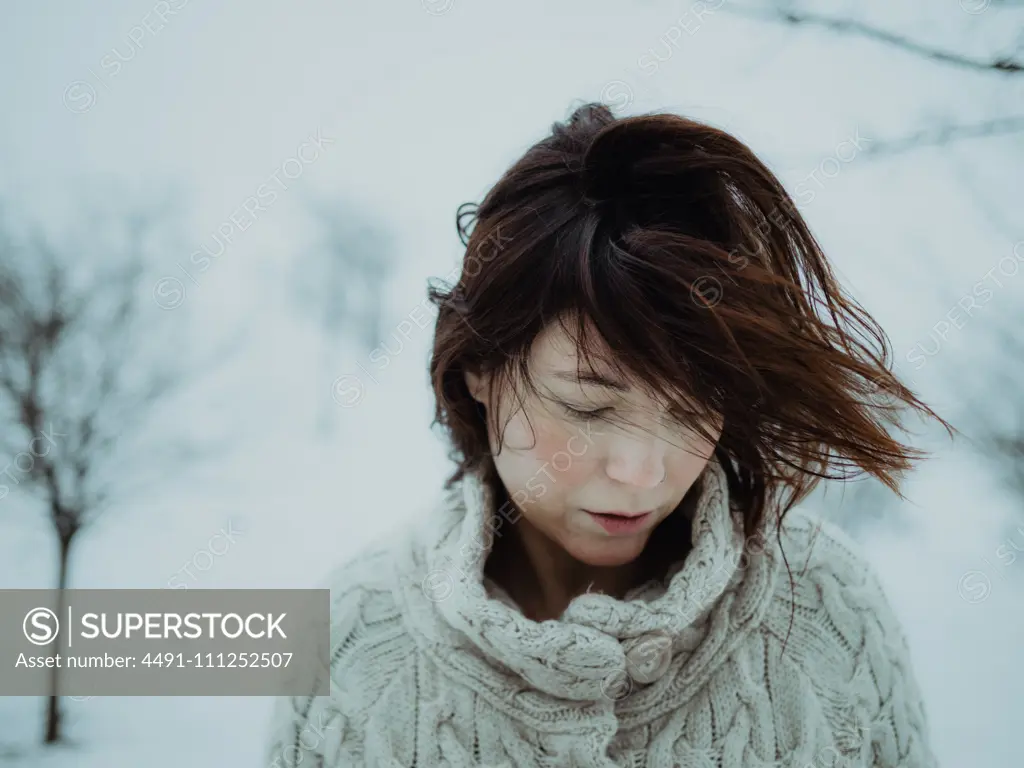 Portrait of pensive attractive brunette in white sweater on background of snowy area