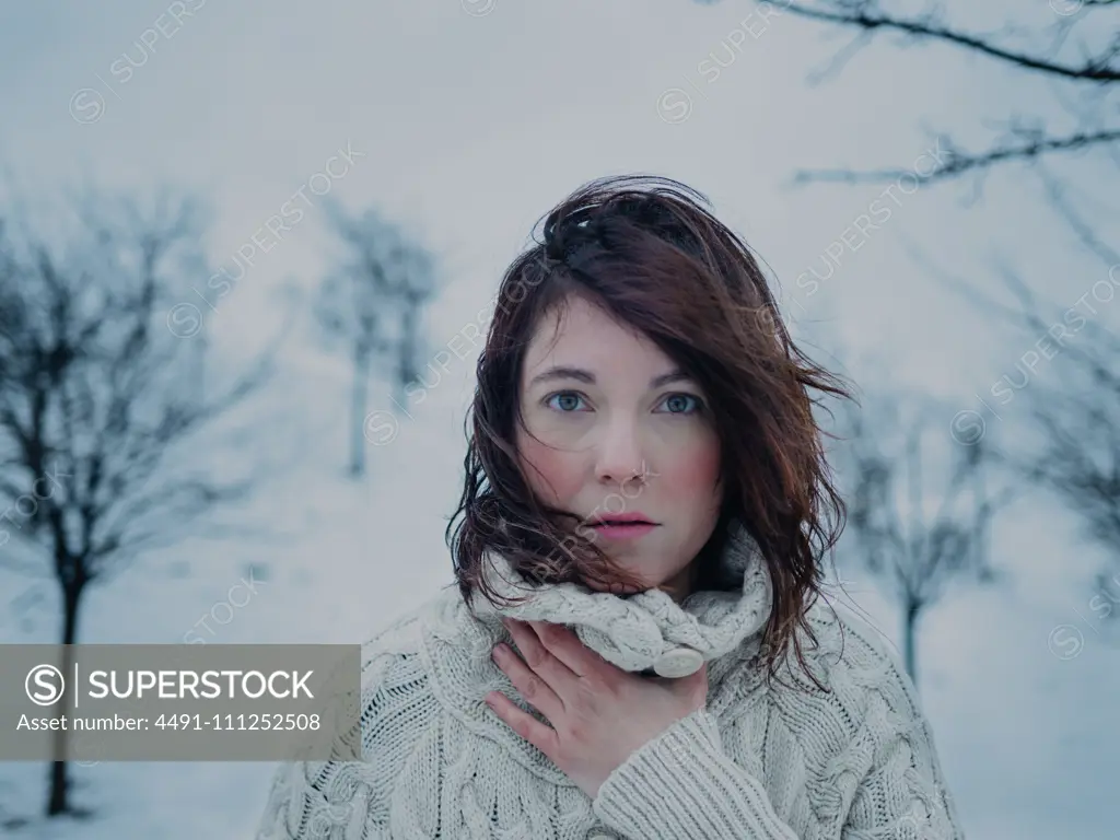 Portrait of pensive attractive brunette in white sweater on background of snowy area