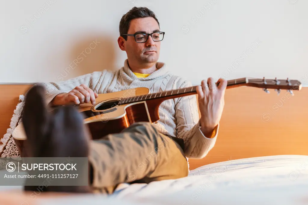 Man playing the guitar on the bed of his house