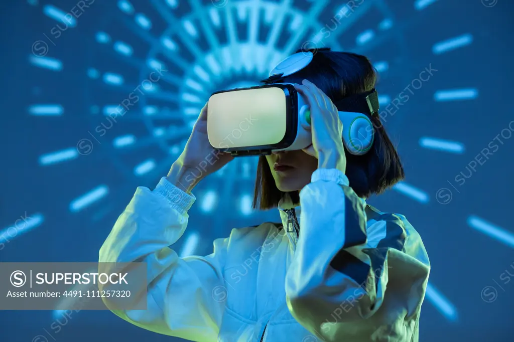 Excited young woman having virtual reality experience in neon light