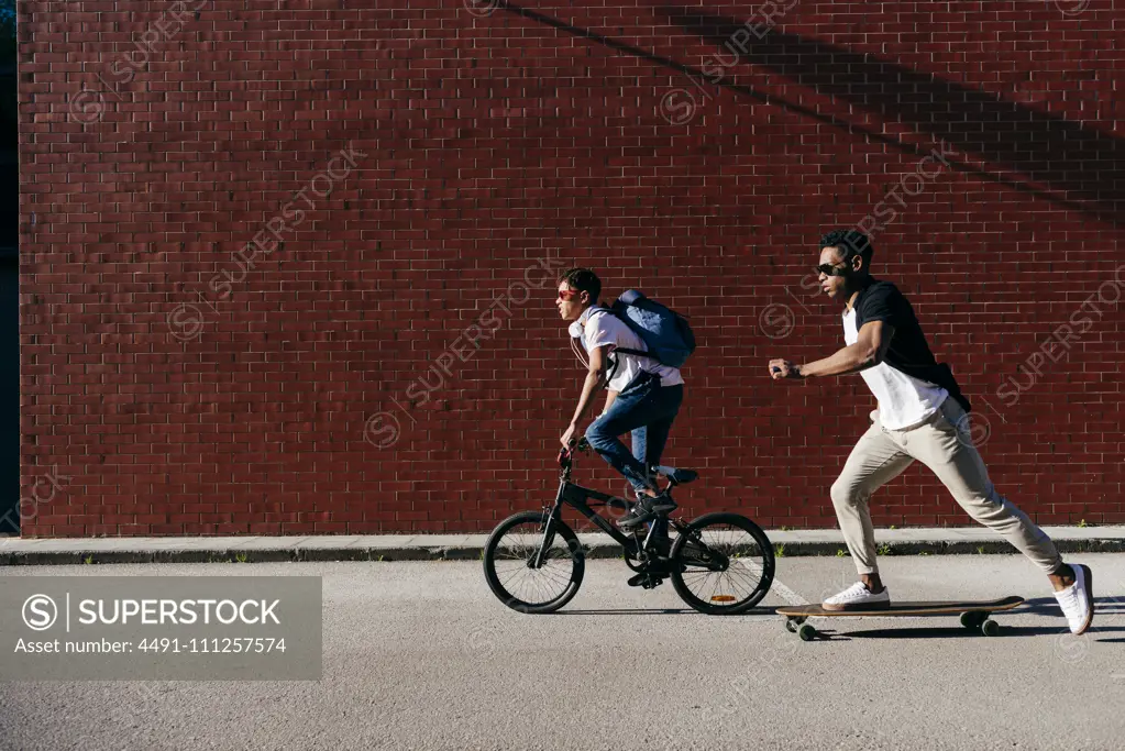 Young African American men riding bicycle and skateboard