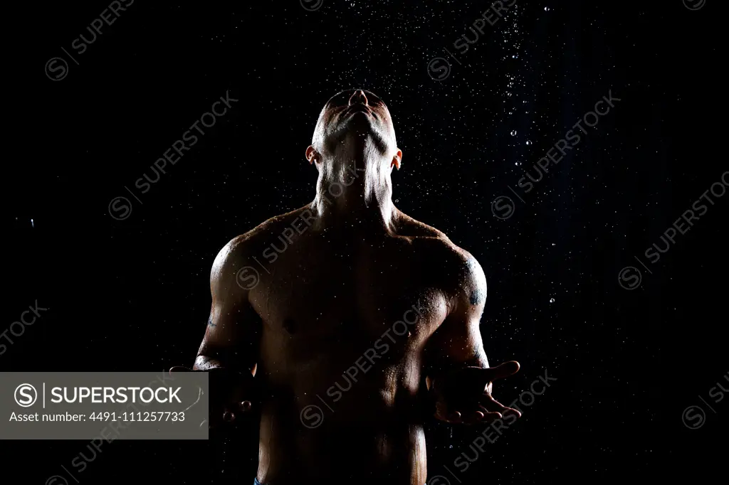 Strong shirtless man looking up and enjoying water drops falling