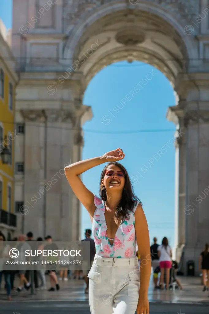 Young happy woman in sunglasses standing beside majestic arch in city street in Lisbon, Portugal