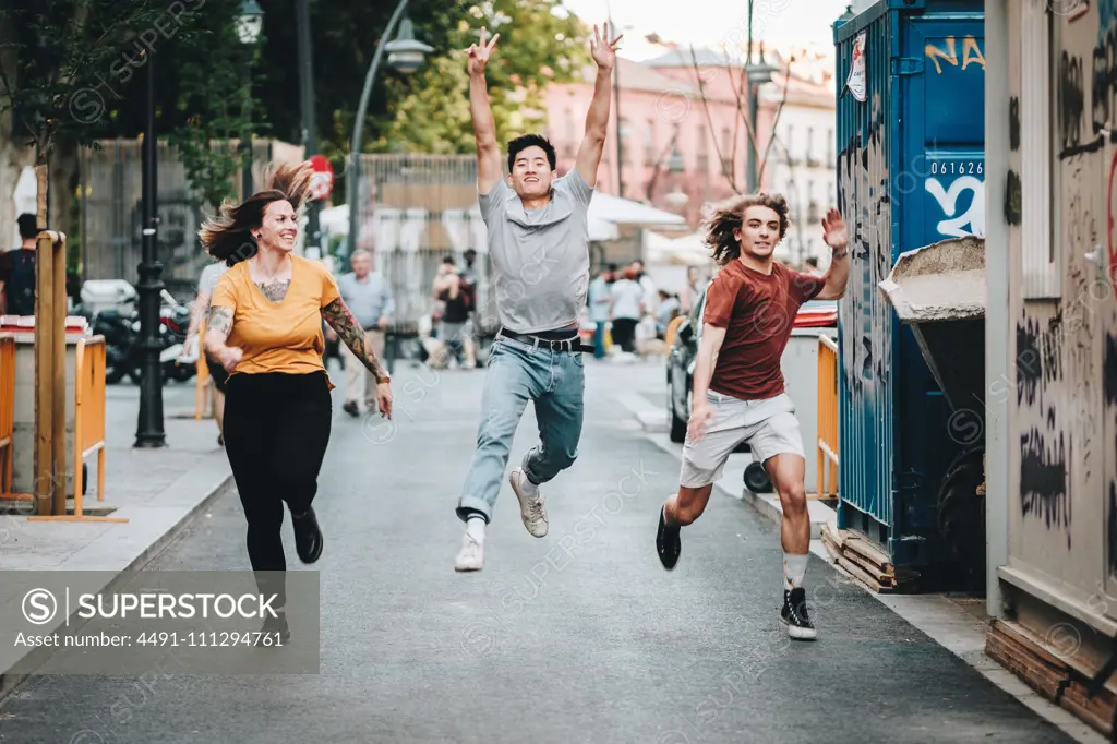 Smiling multiethnic competitive people in casual clothes hurrying and running along urban street