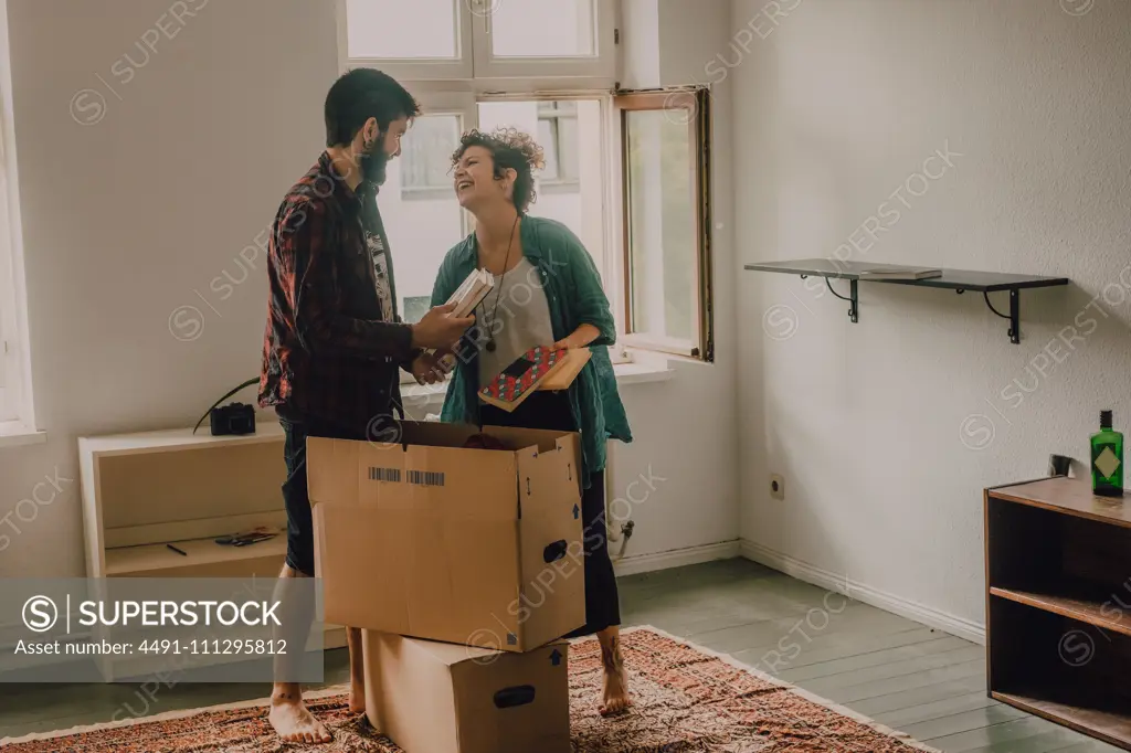 Hipster couple unpacking together boxes while standing barefoot in light room