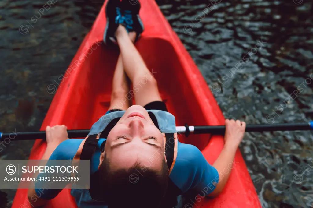 Back view of sportswoman sitting in red canoe and raising paddle on Sella river decline in Spain 