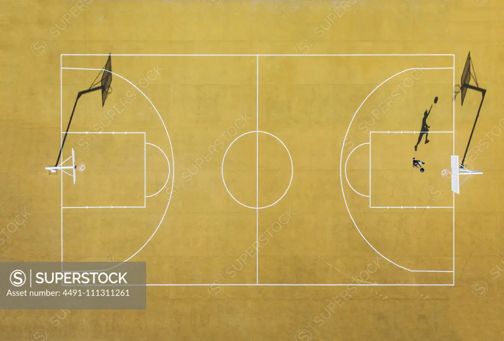 Young man playing basketball on outdoor court. Top view, bird eye view of yellow basketball court