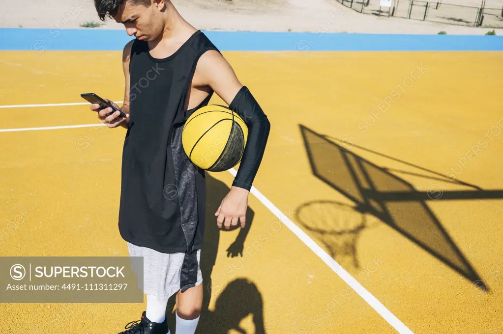 Male basketball player using his smartphone resting after training session. 