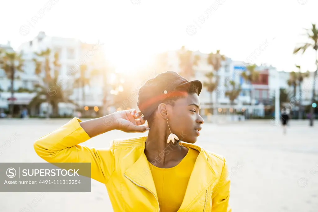 Portrait of African American woman in stylish bright jacket looking away on sandy beach blurred background 