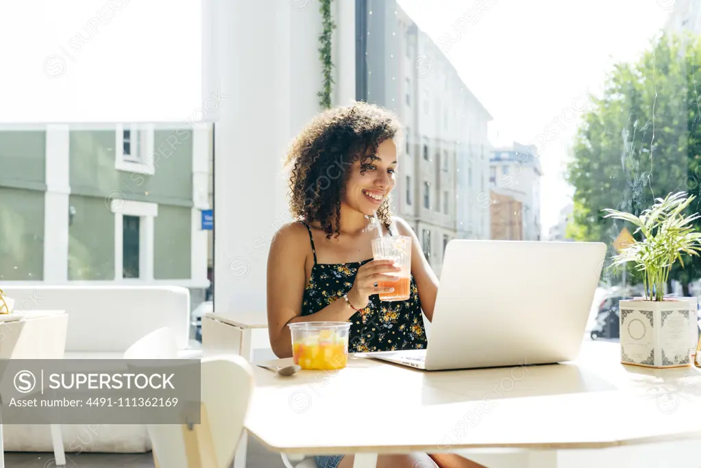 Ethnic female with laptop enjoying healthy drink in cafe