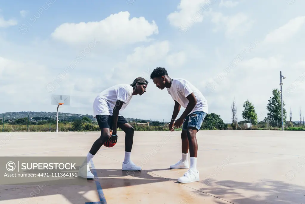 Side view of African American guys playing basketball in bright day on play ground