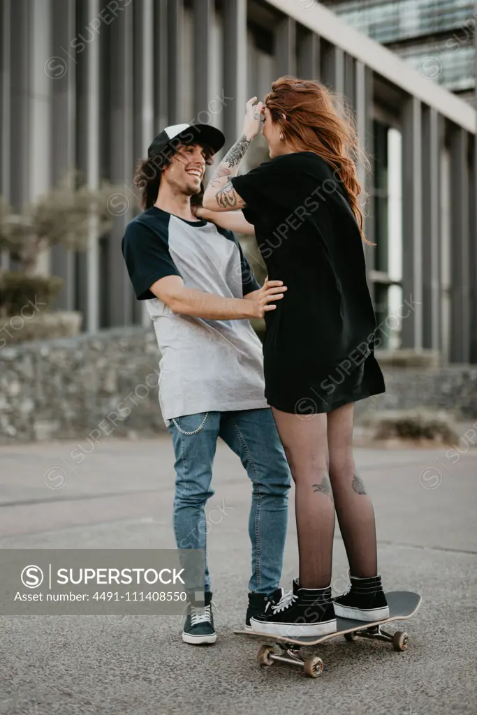 Laughing teenage guy and girl learning to skate having fun on street