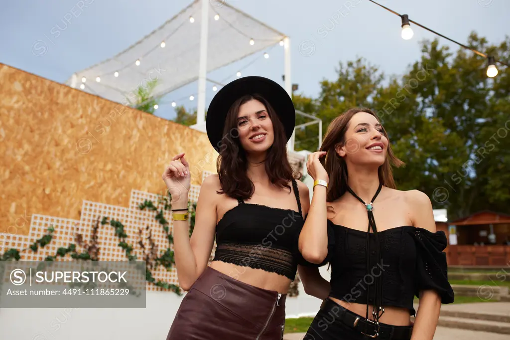 Charming long haired stylish girl friends having fun in bright day at festival