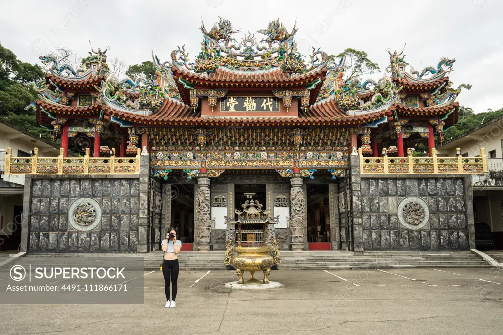 Female traveler in casual wear taking picture in front of camera with beautiful Taoist Temple Dai Quan Tang at Taiwan;Female tourist with photo camera visiting aged oriental temple