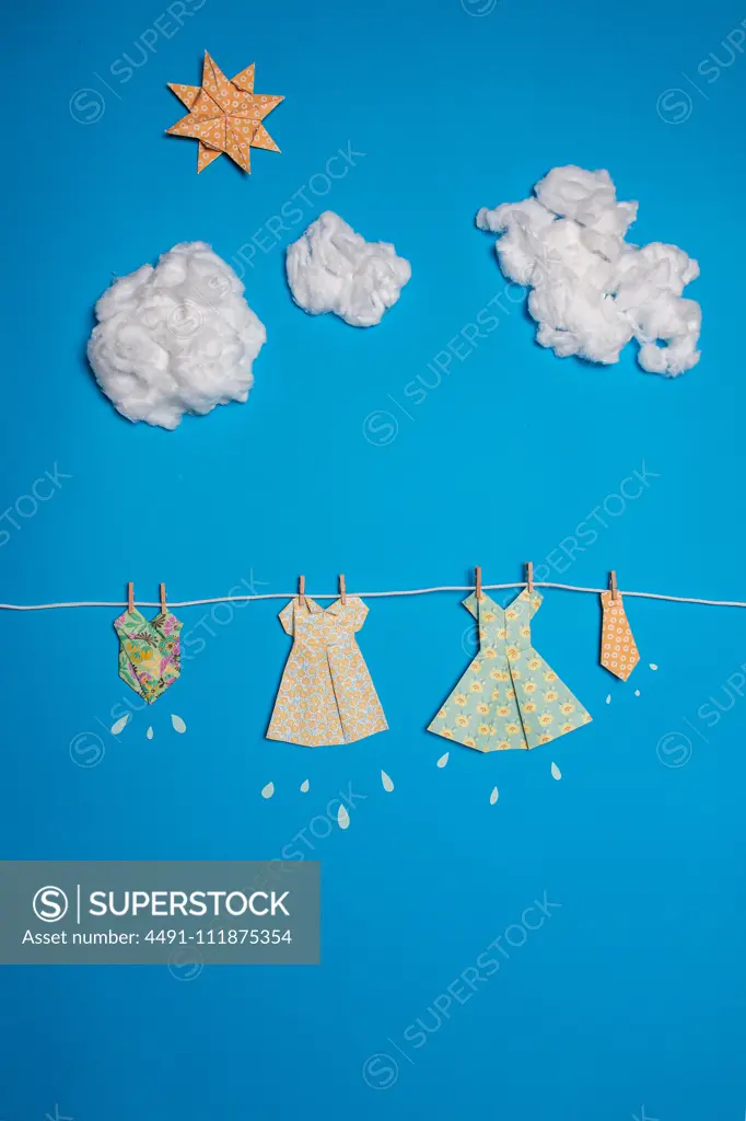 Cute paper dresses attached to rope against blue sky with clouds