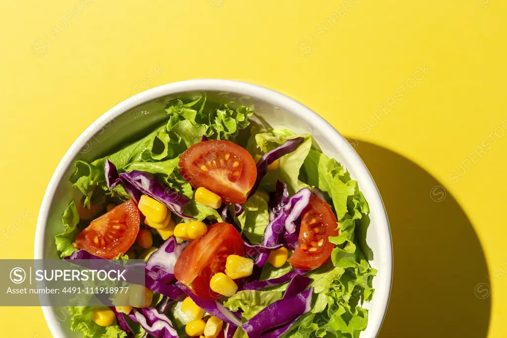 Fresh lettuce salad with Cherries tomatoes, red onion and corn, sunlight on pink background from above. Healthy food. Vegan food.