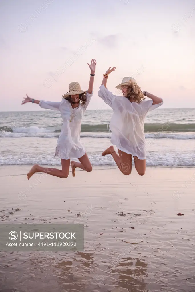 Smiling girlfriends in summer clothes barefoot in water on beach