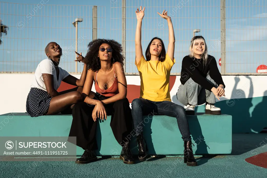 Careless youthful diverse women in casual clothes having fun together on stadium