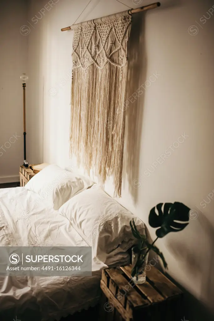 Vintage macrame decoration hanging on wall over comfortable bed in cozy bedroom at home