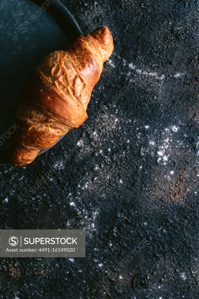 Top view of soft fresh bun placed on metal tray on messy black table during breakfast