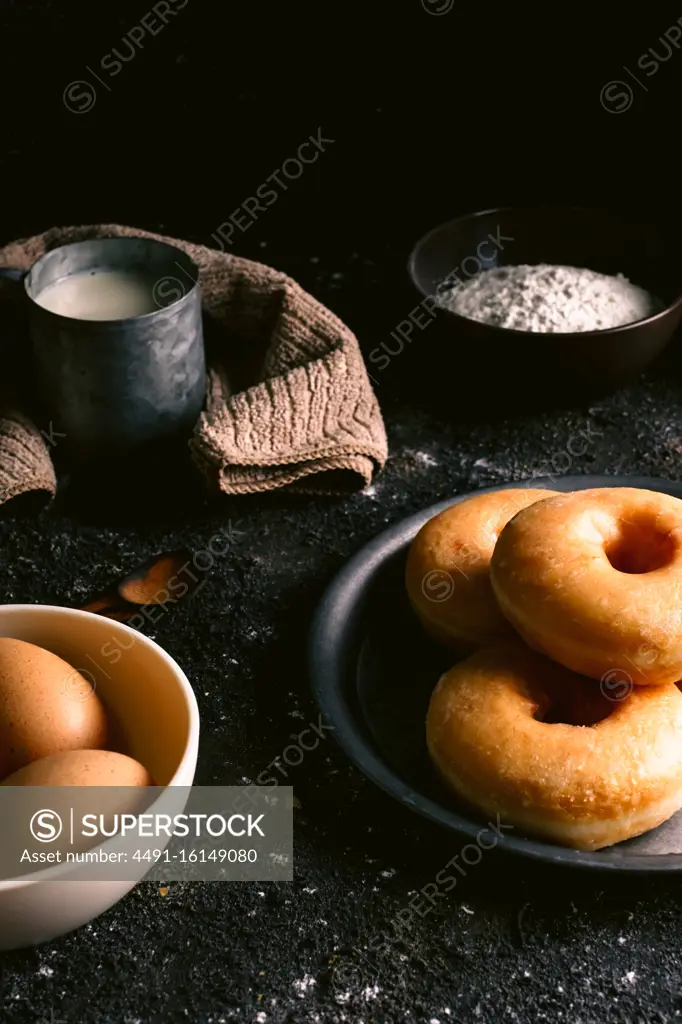 Fresh doughnuts placed on rough table near various pastry ingredients and utensils in kitchen